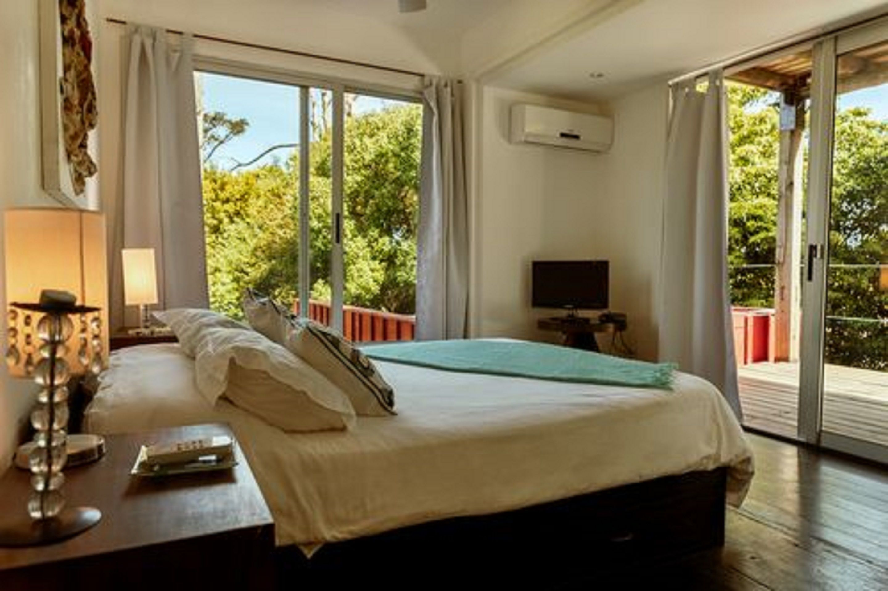 Une chambre avec un lit, une télévision et un balcon donnant sur la forêt.