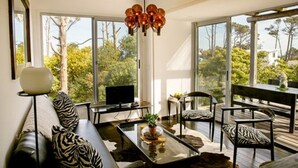 A modern living room with a glass coffee table, a sofa with zebra print cushions, a television, and a dining area with chairs and a table. - CDL - containers design loft (José Ignacio)