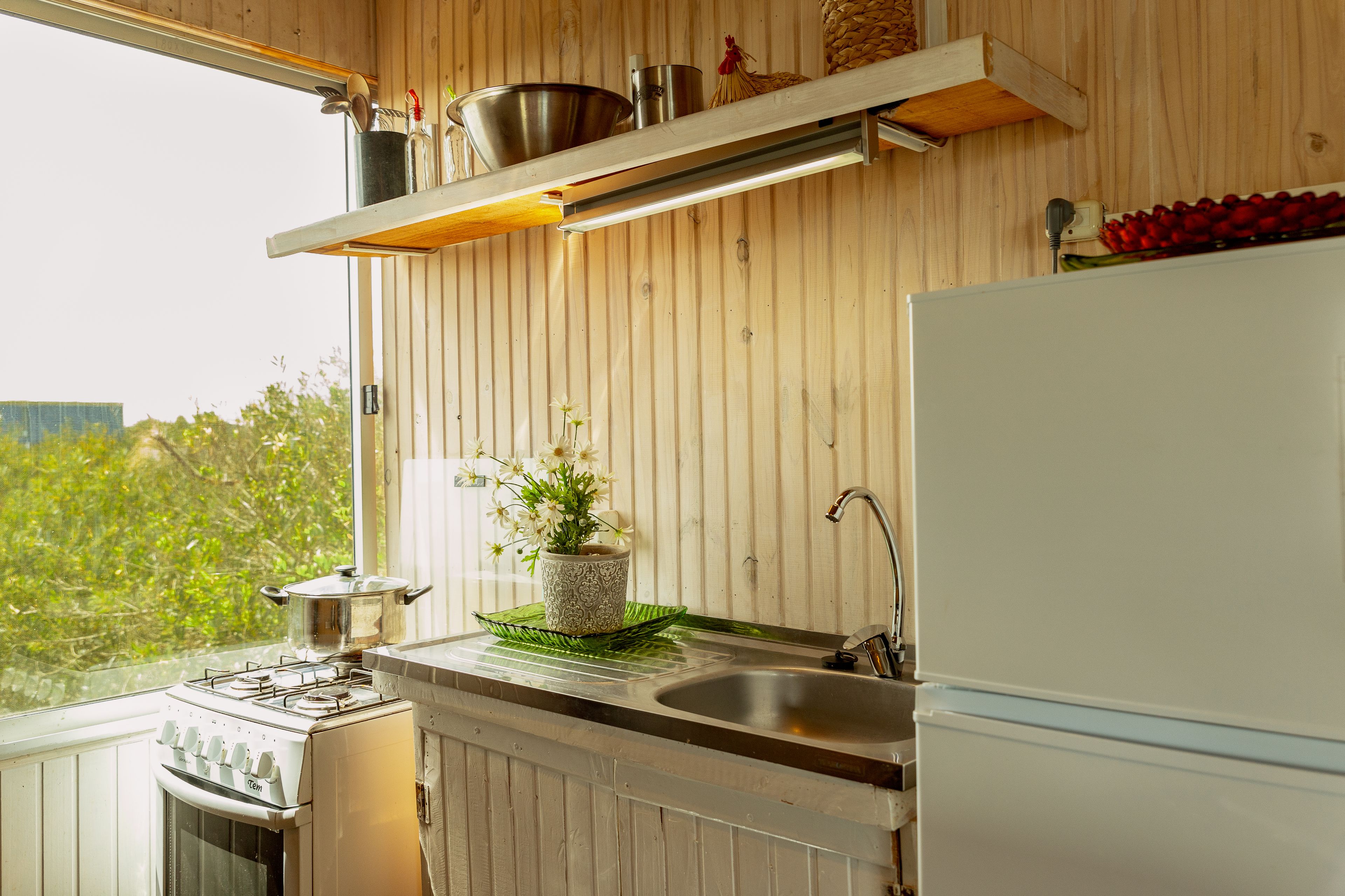 A kitchen with wooden paneling, a stove, a sink, and a refrigerator.