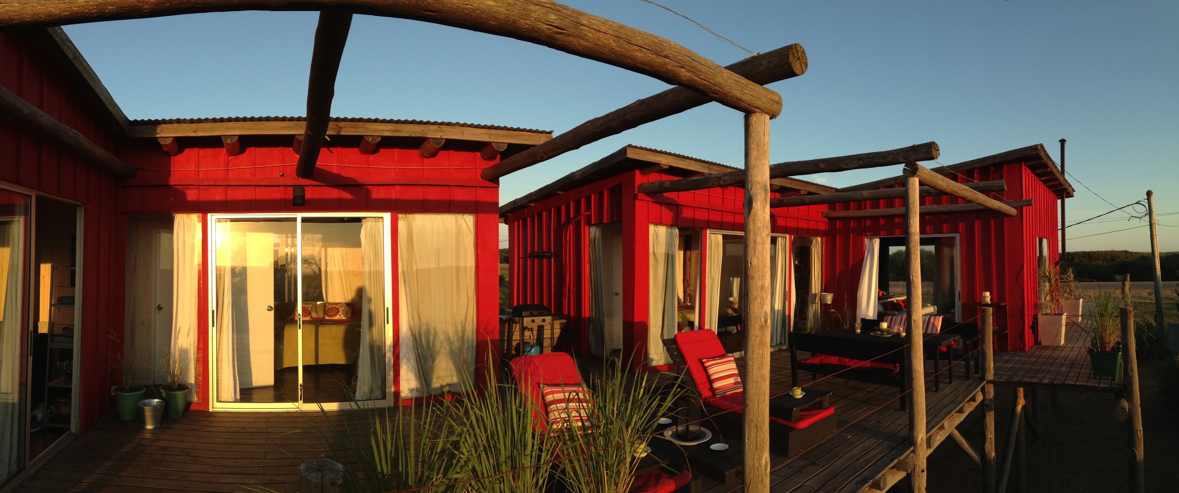 A red building with a wooden deck, glass doors, and outdoor seating.