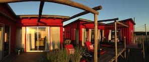A red building with a wooden deck, glass doors, and outdoor seating. - BDL - beach design loft (José Ignacio)