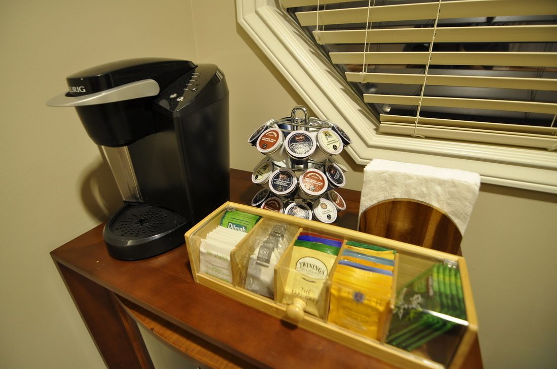 A coffee maker, a tray of coffee pods, and a box of tea bags on a wooden table.