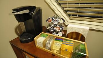 A coffee maker, a tray of coffee pods, and a box of tea bags on a wooden table.