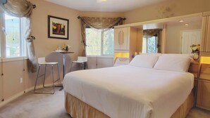 A bedroom with a large bed, a desk, and a chair. There is a window with curtains, a framed picture on the wall, and a mirror. - Cornerstone Bed and Breakfast (Revelstoke)