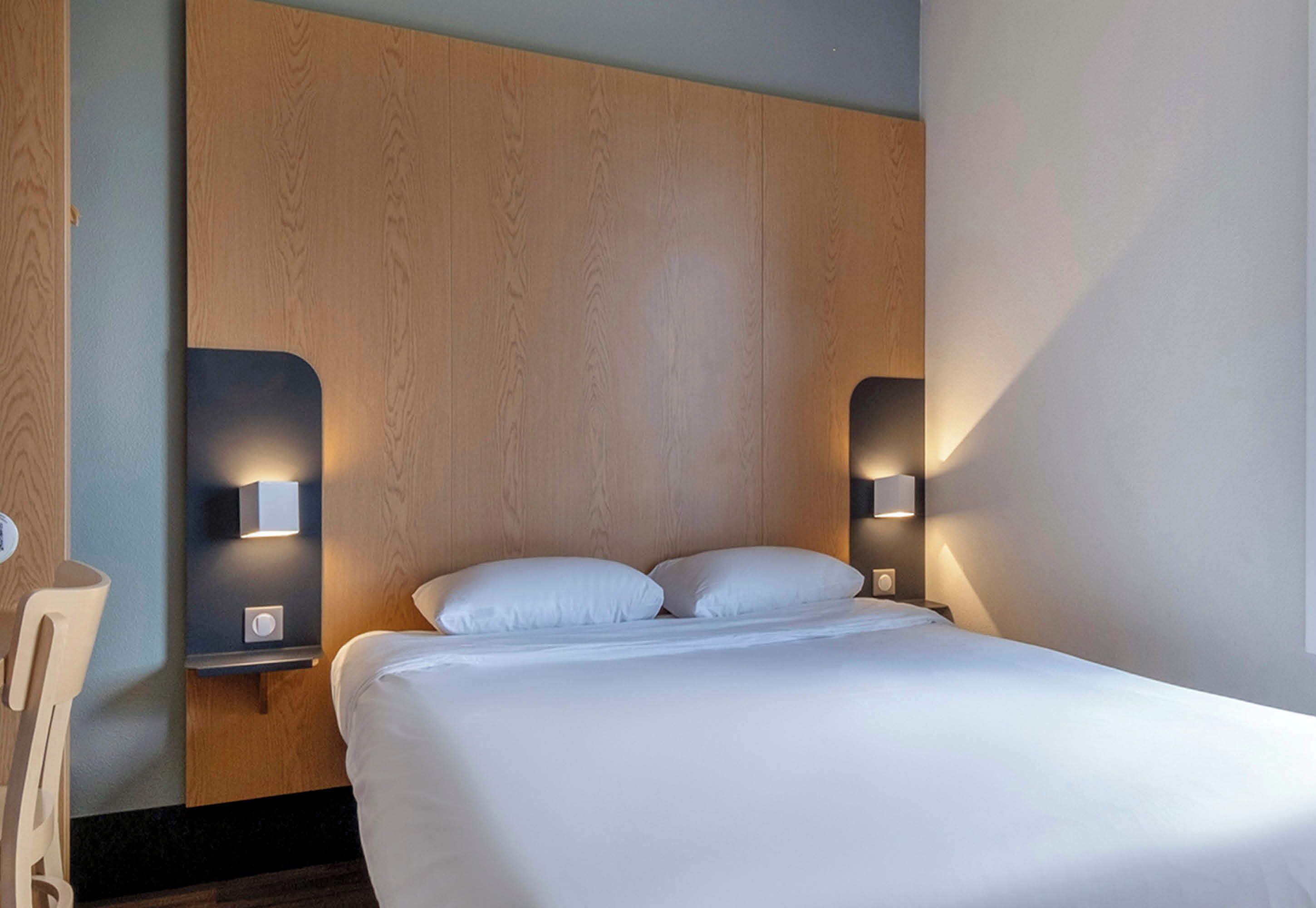 A hotel room with a wooden headboard, two bedside lamps, and a neatly made bed.
