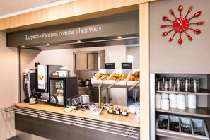 Un espace buffet pour le petit-déjeuner avec une machine à café, des viennoiseries et divers plats proposés dans des récipients.