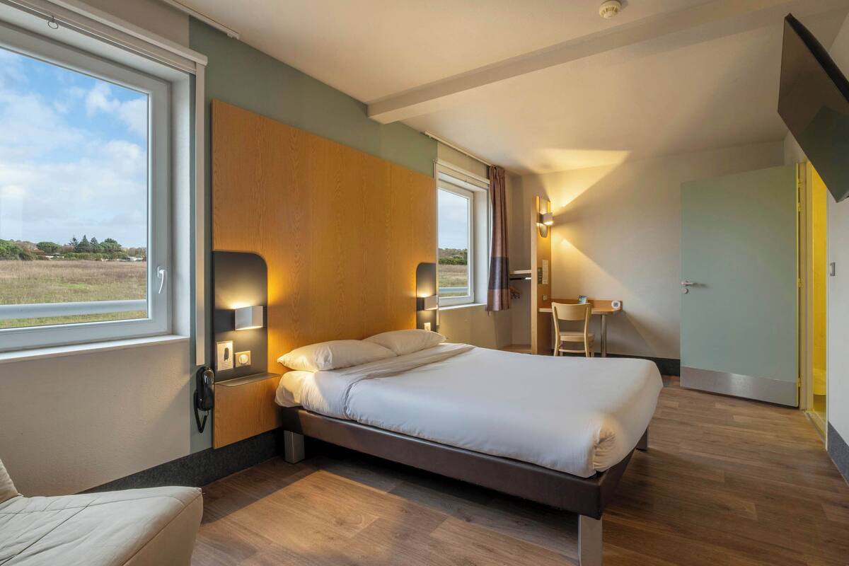 Un dormitorio moderno con una cama grande, mesitas de noche, un escritorio y una silla. Se ve una ventana que ofrece vistas al exterior.