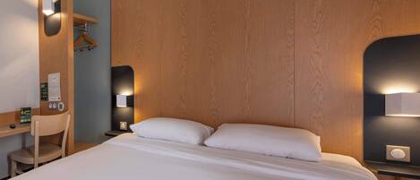 Habitación de hotel con una cama grande, cabecera de madera, escritorio con una silla y mesita de noche con lámpara.