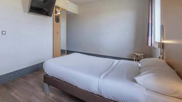 Une chambre d’hôtel moderne équipée d’un lit, d’un téléviseur à écran plat fixé au mur, d’une petite table de chevet et d’une fenêtre avec des rideaux.