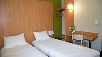 A hotel room with two beds, a desk, a chair, a lamp, and a wall-mounted light.