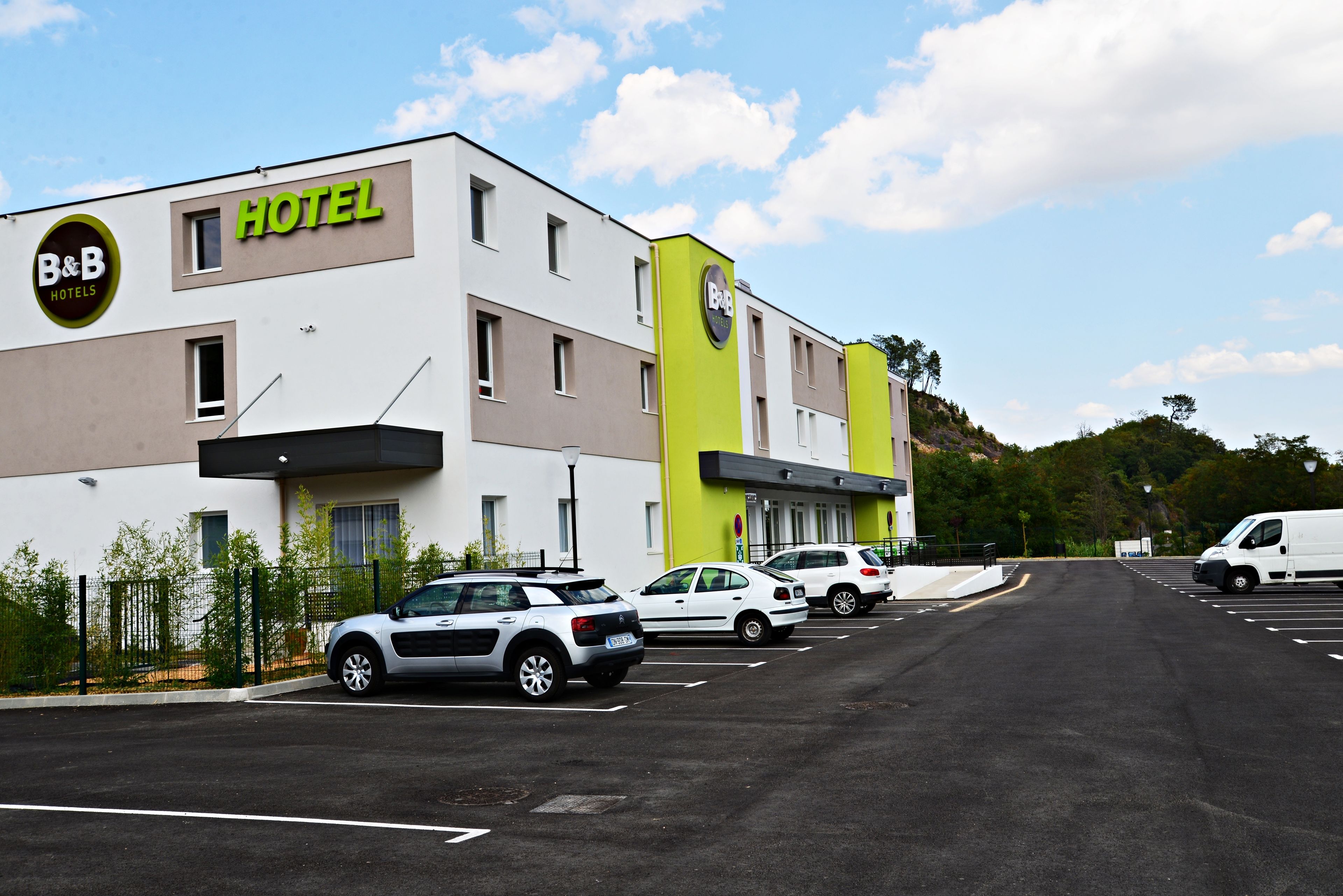 Un hôtel-restaurant de type « bed and breakfast » au design moderne, doté d’un parking où sont stationnées plusieurs voitures et d’un fourgon blanc.