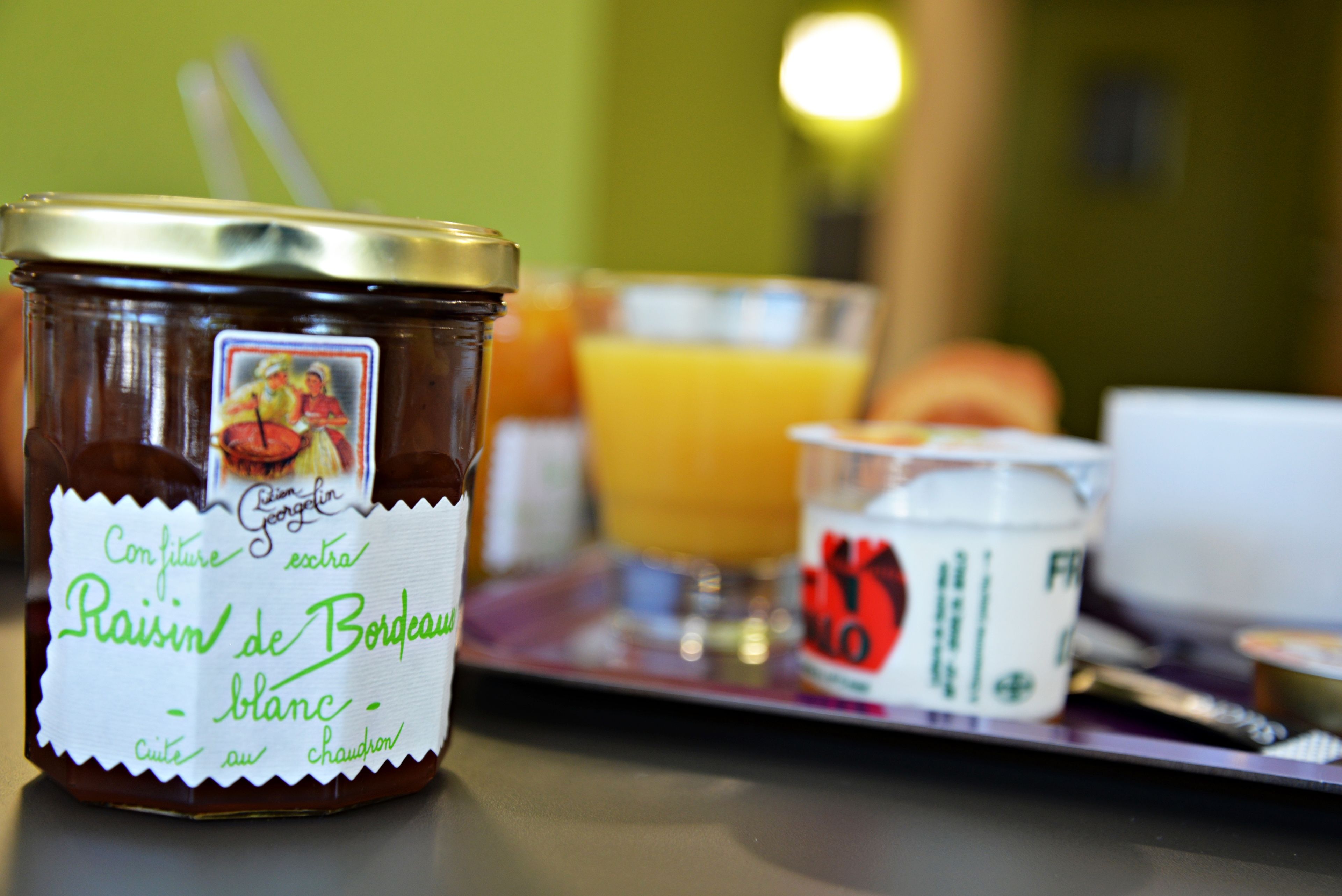 Et glas Confiture extra Raisin de Bordeaux blanc på et fad med et glas appelsinjuice og en lille skål yoghurt.