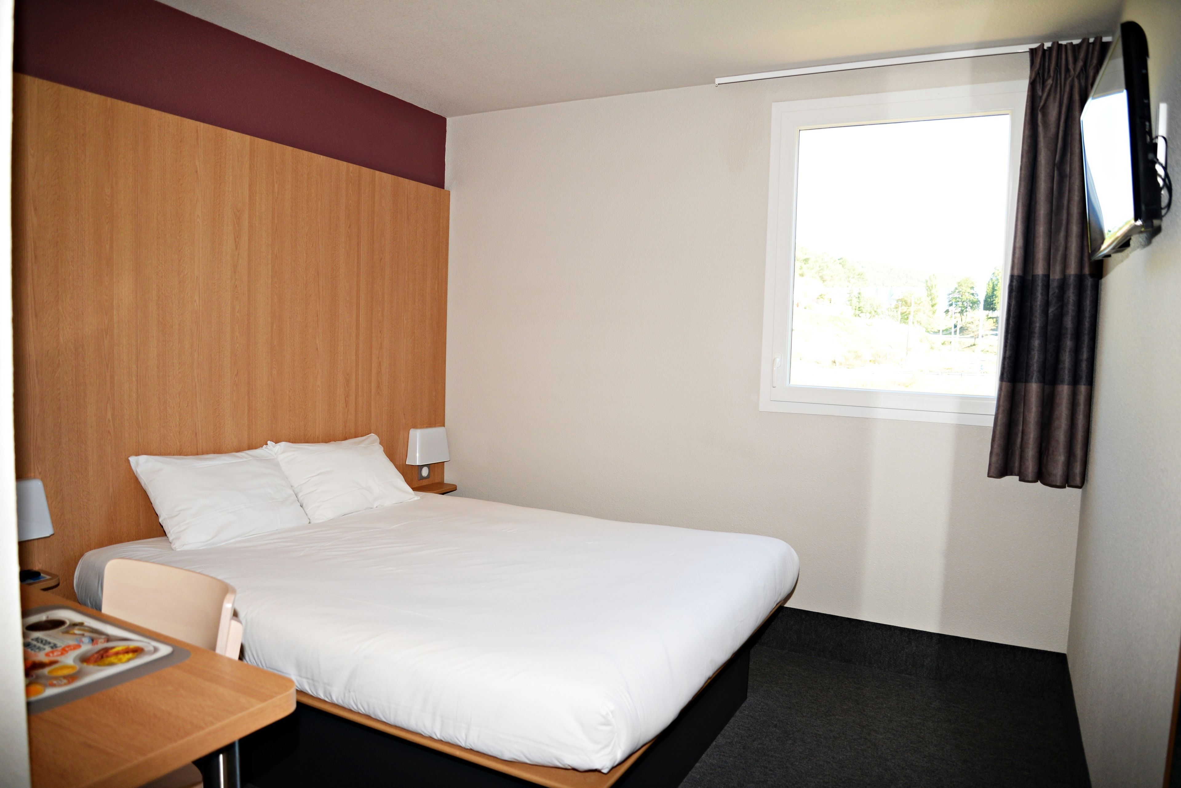 Una habitación de hotel con cama, escritorio y ventana con cortinas.