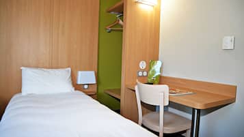 A hotel room with a bed, a desk, a chair, a lamp, and a wall-mounted light fixture.