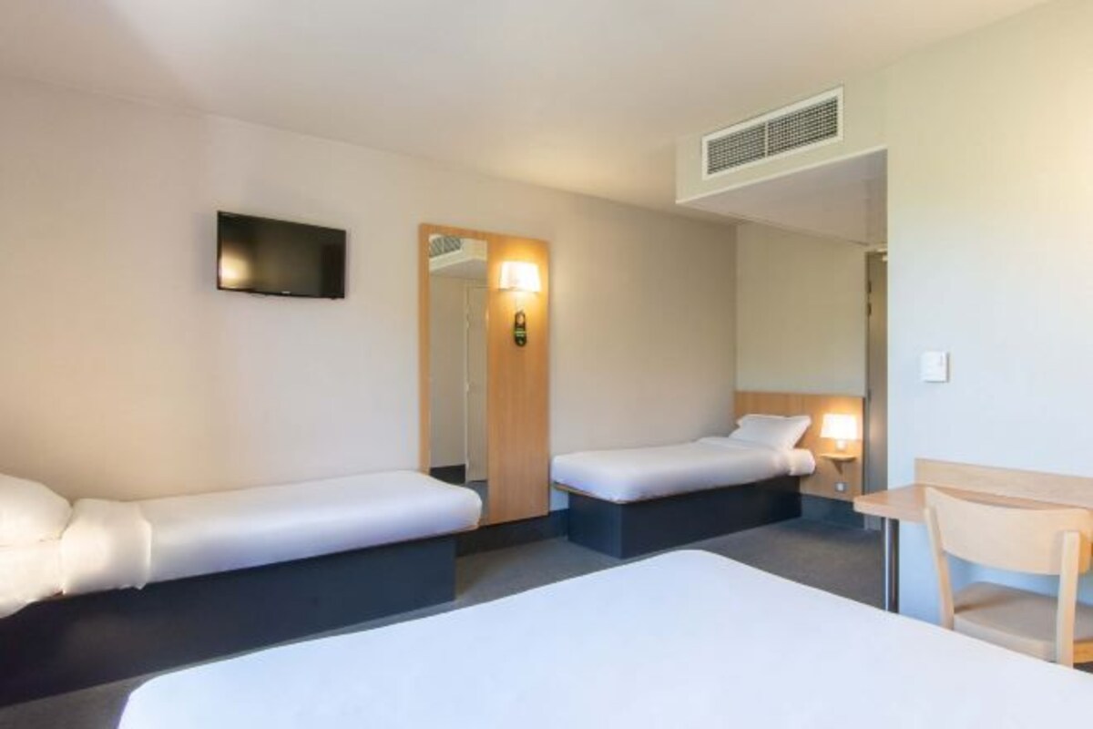A hotel room with two single beds, a desk, a chair, a TV, and a mirror.
