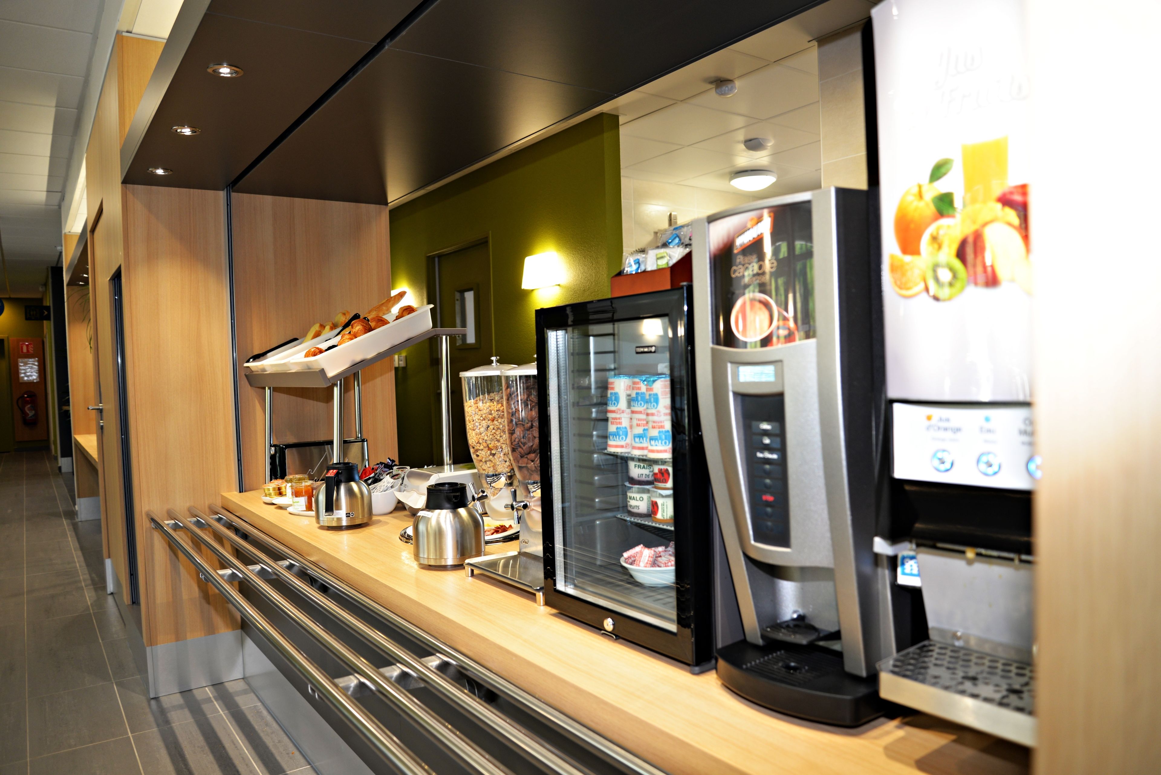 A self-service breakfast bar with a coffee machine, a refrigerated display case, and a beverage dispenser.