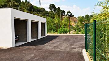 Un edificio moderno con tres puertas de garaje, un camino de entrada pavimentado y una cerca verde.