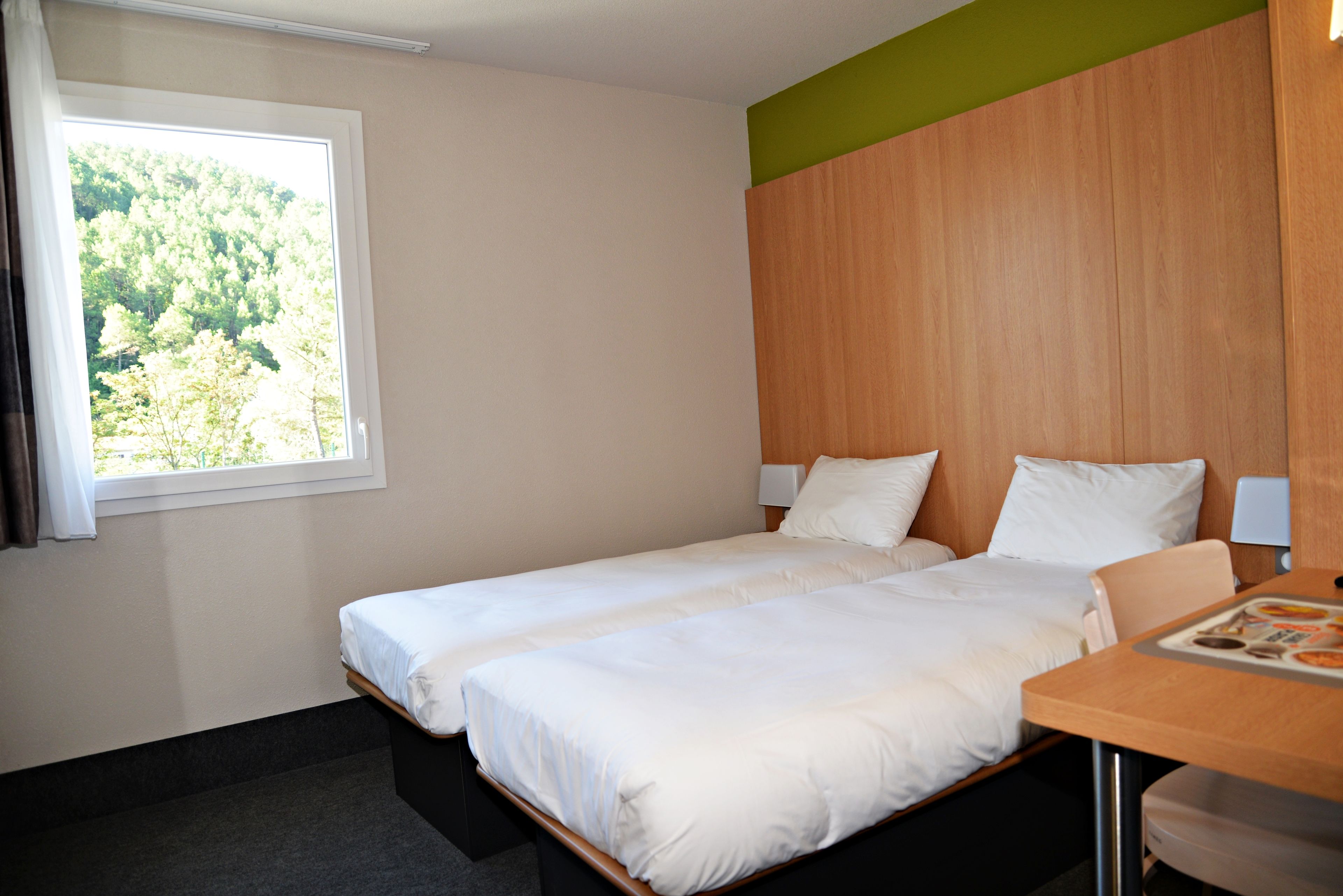 Een hotelkamer met twee bedden, een raam met uitzicht op bomen en een houten hoofdeinde.