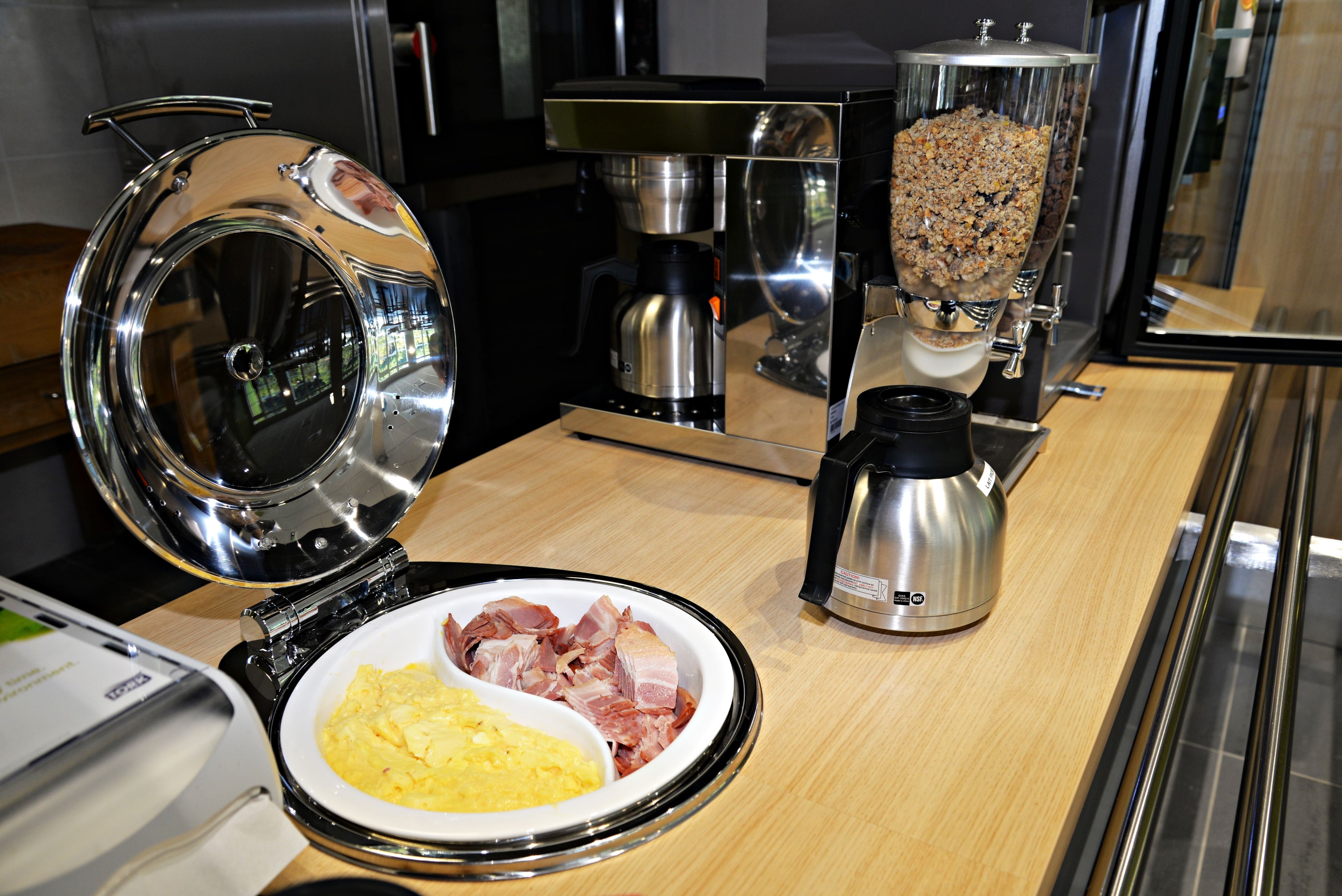 Un plan de travail de cuisine avec une machine à café, un robot culinaire et une assiette contenant des œufs brouillés et du bacon.