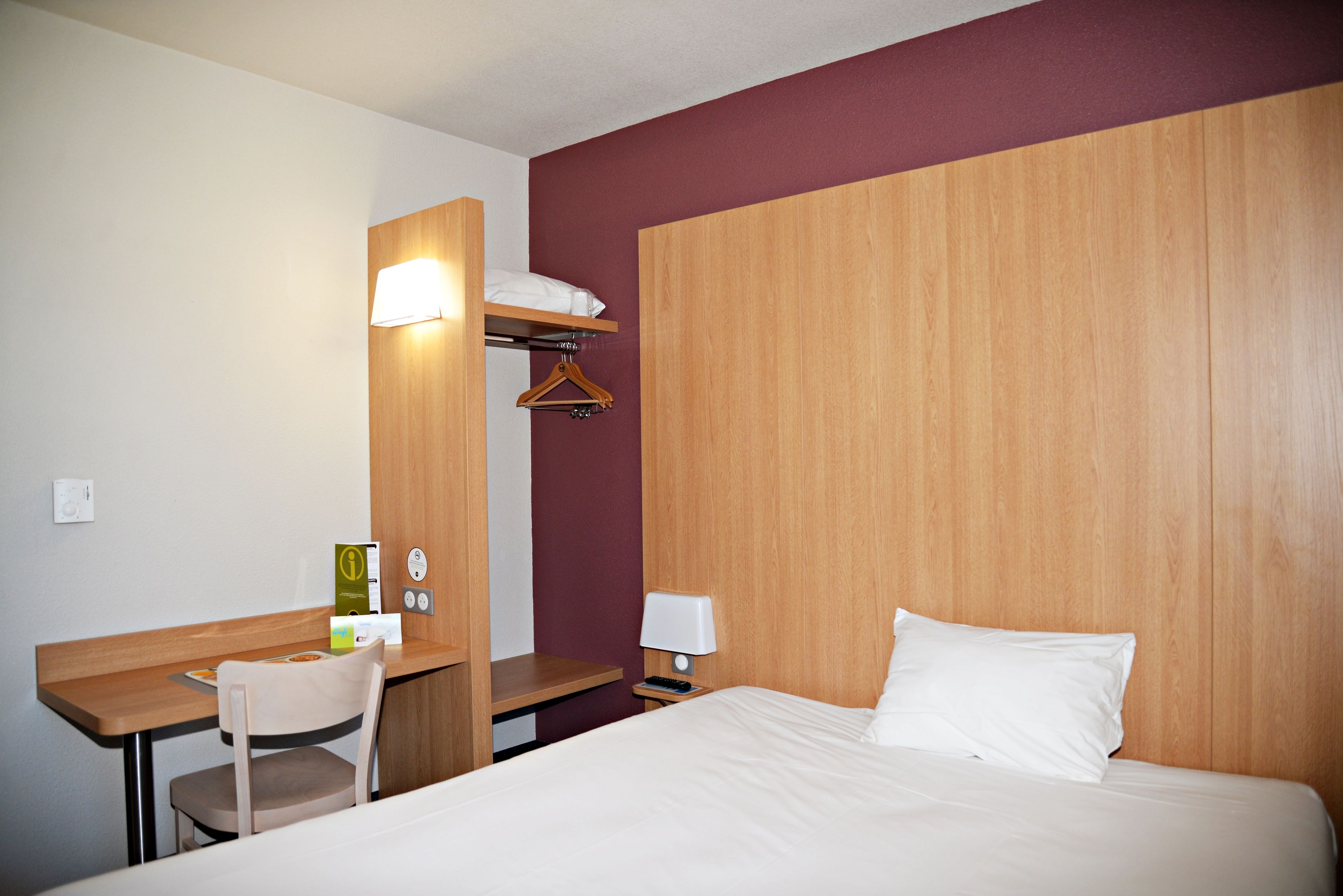 Ein Hotelzimmer mit einem Bett, einem Schreibtisch, einem Stuhl, einem Kleiderhaken und einer Wandlampe.