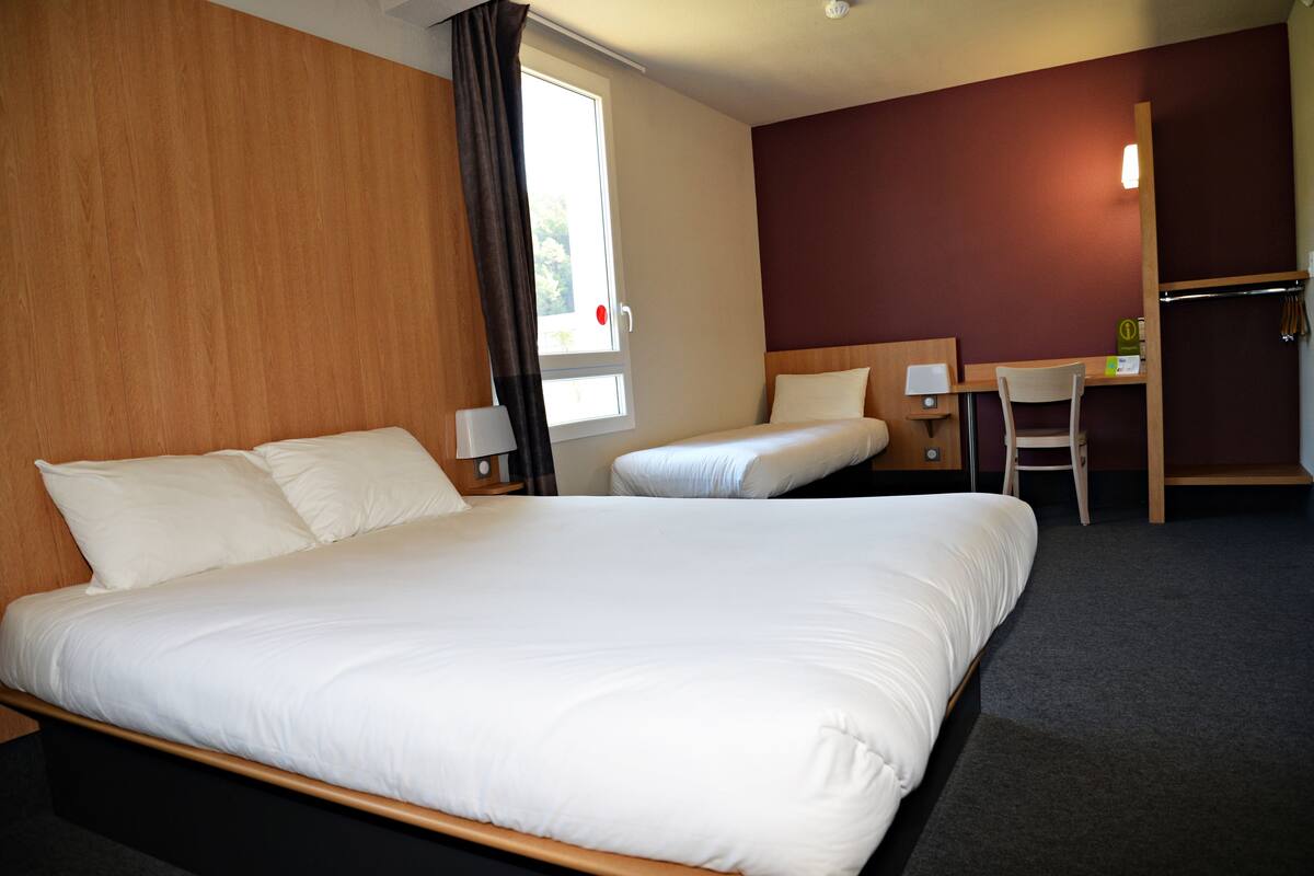 Ein Hotelzimmer mit einem großen Bett, einem kleineren Bett, einem Schreibtisch und einem Sessel.