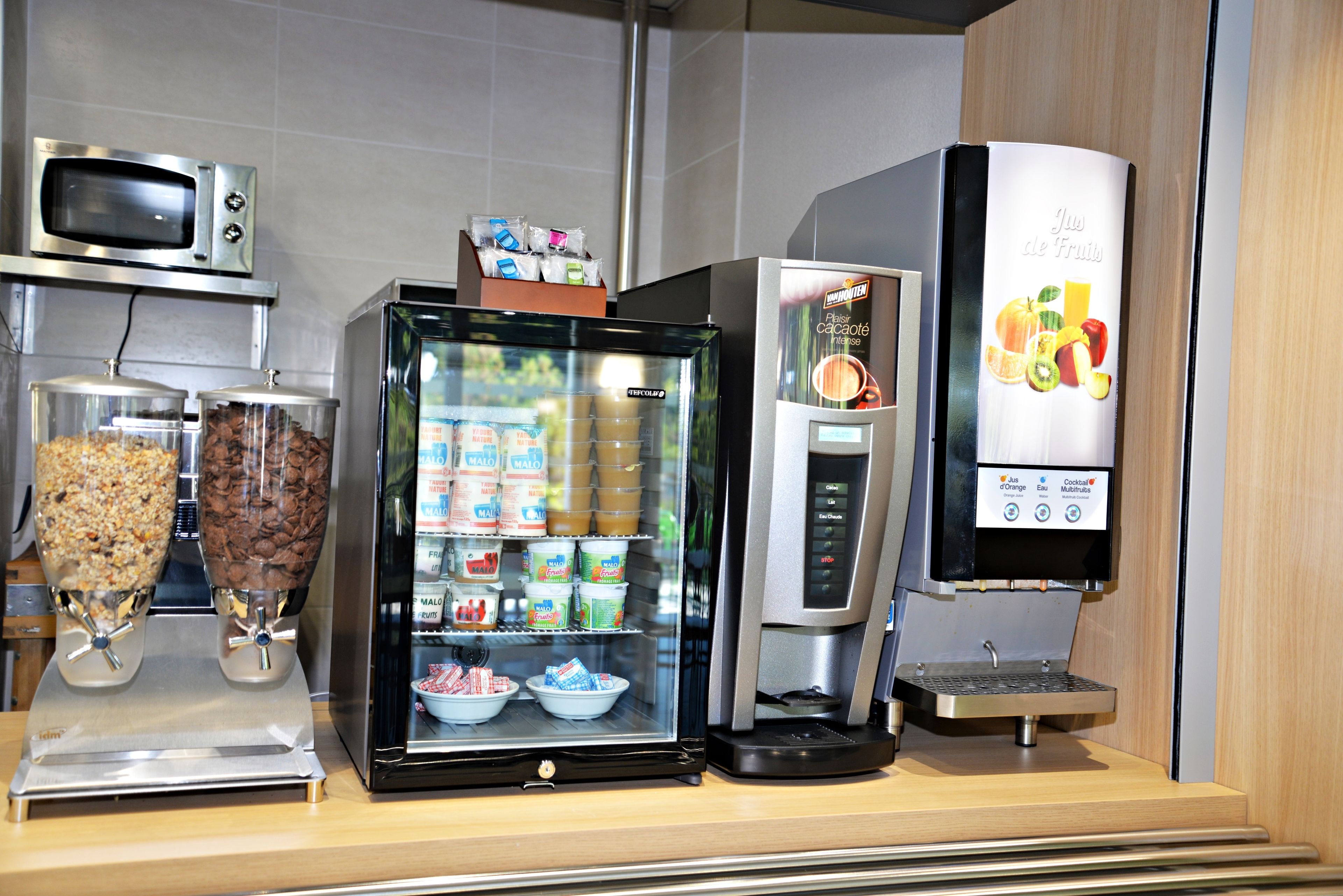 Una estación de bebidas de autoservicio con una máquina de café, un refrigerador y un microondas.