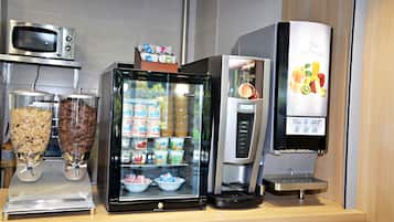 Una estación de bebidas de autoservicio con una máquina de café, un refrigerador y un microondas.