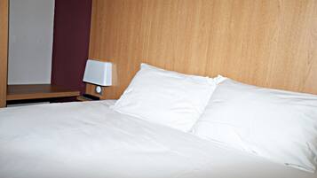 Una cama bien hecha con sábanas blancas, un cabecero de madera y una mesita de noche con una lámpara.