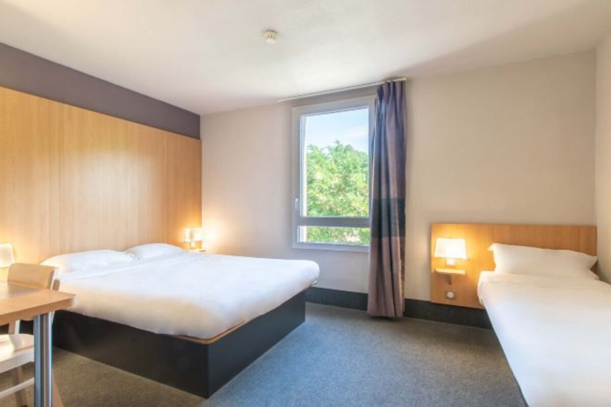 A hotel room with a bed, a desk, and a window with curtains.