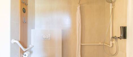 A modern bathroom with a shower, toilet, and handrails.