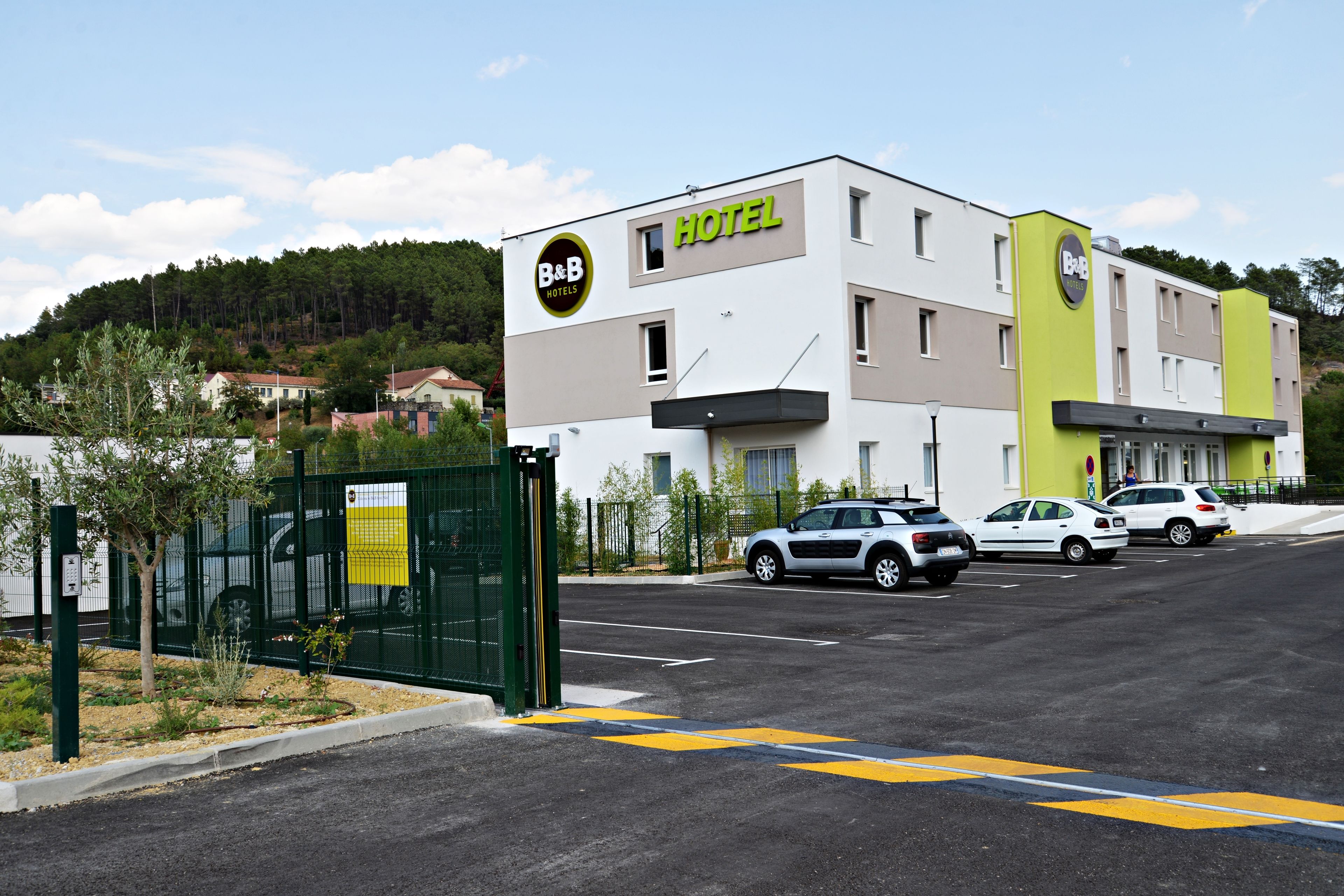 A B&B hotel with a modern design, a parking lot, and a green fence.