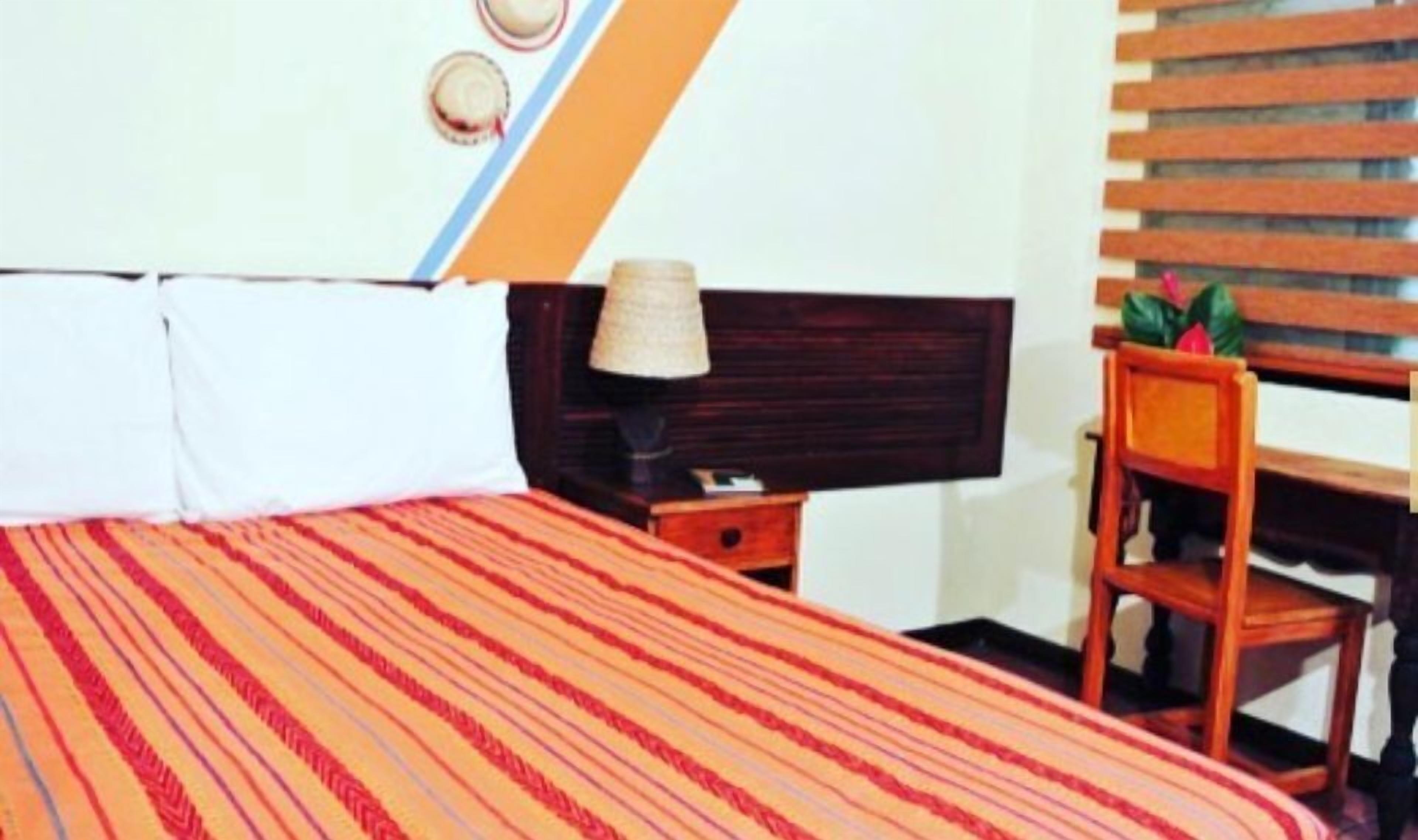 Una habitación de hotel con cama, mesita de noche, una silla y televisión montada en la pared.