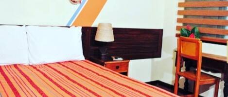 Una habitación de hotel con cama, mesita de noche, una silla y televisión montada en la pared.