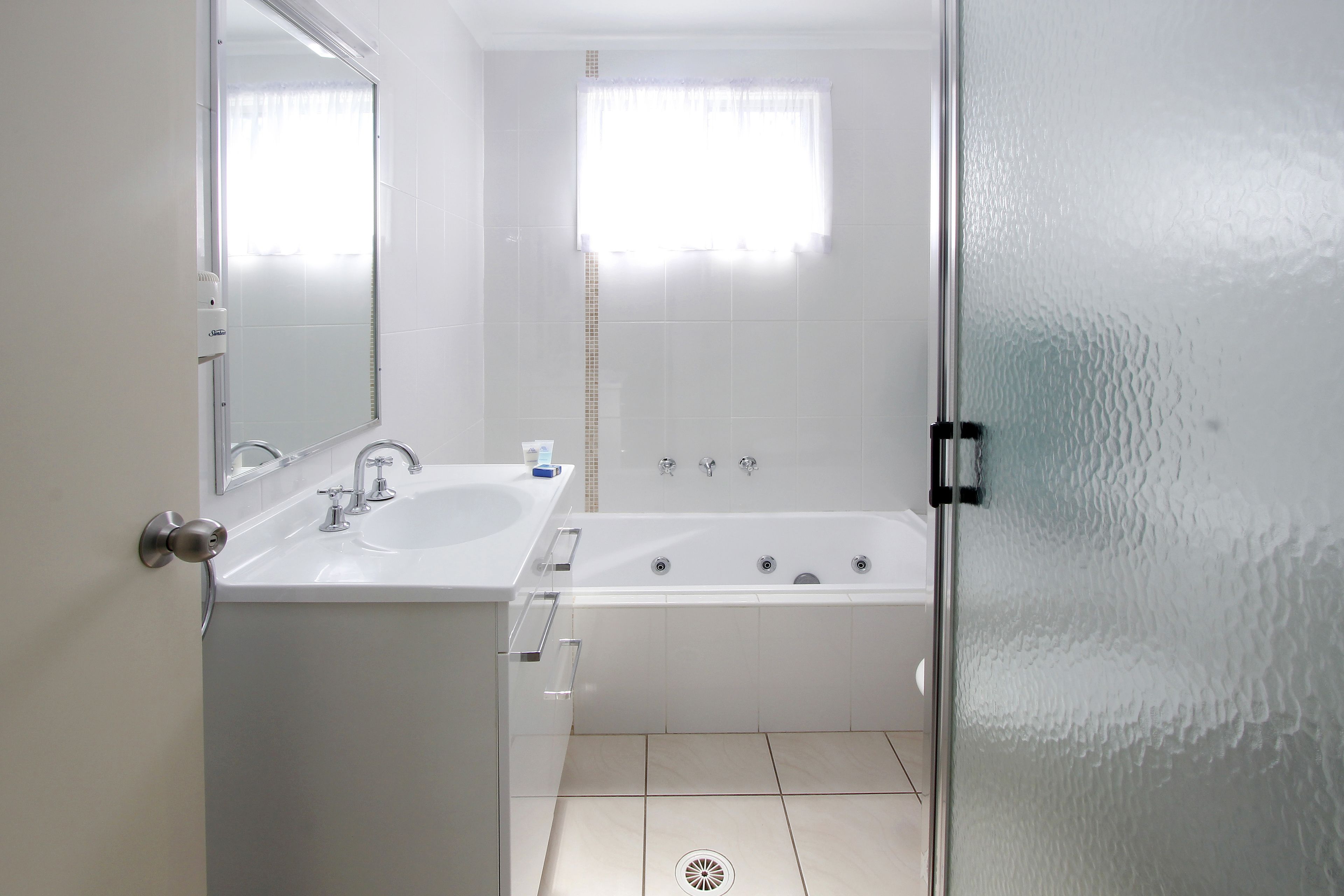 Un baño con un lavamanos blanco, una bañera, un espejo y una ventana con cortina.