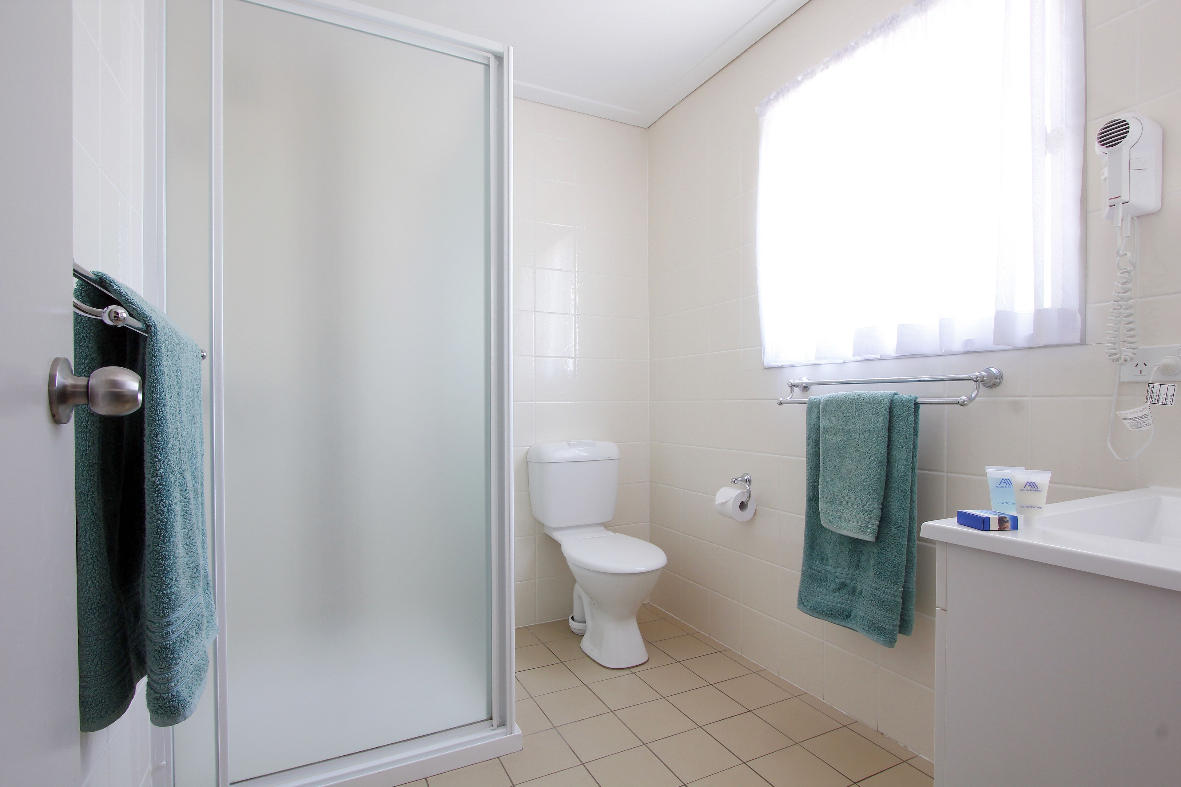 A bathroom with a toilet, a sink, a towel rack, and a shower door.