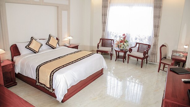 Une chambre d’hôtel avec un grand lit, deux tables de chevet, un bureau avec une chaise et une fenêtre avec des rideaux.