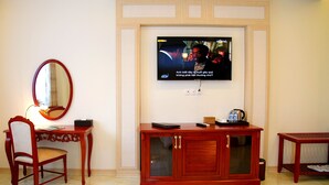 Une chambre d’hôtel avec un bureau en bois, une chaise, un téléviseur fixé au mur et une petite table sur laquelle sont posées des chaussures.