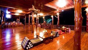 An indoor wooden deck with seating and tables, a television, and a view of the night sky. - Haad Yao Over Bay Resort (Ko Pha-ngan)