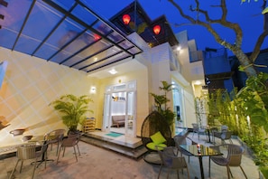 A modern hotel with a glass facade, outdoor seating area, and a visible entrance. - Hoi An Merrily Homestay (Da Nang)