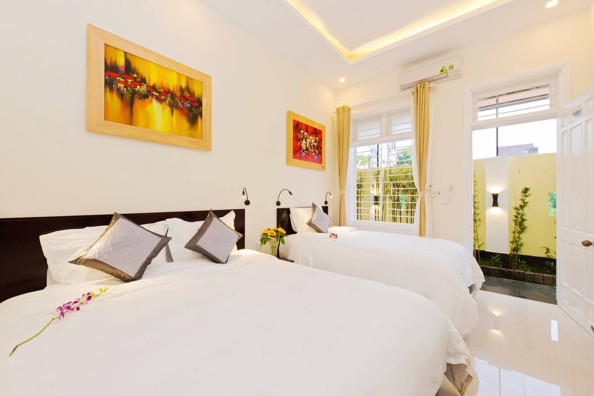 A hotel room with two beds, a painting on the wall, and a window with curtains.