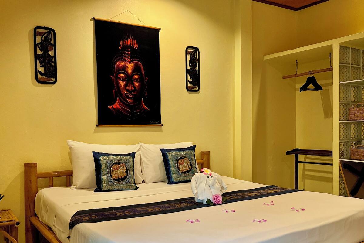 A room with a bed, a wooden headboard, a wall-mounted Buddha painting, and a small shelf with a basket.