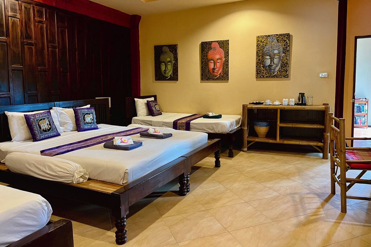 A hotel room with a large bed, two smaller beds, a wooden nightstand, and a chair.