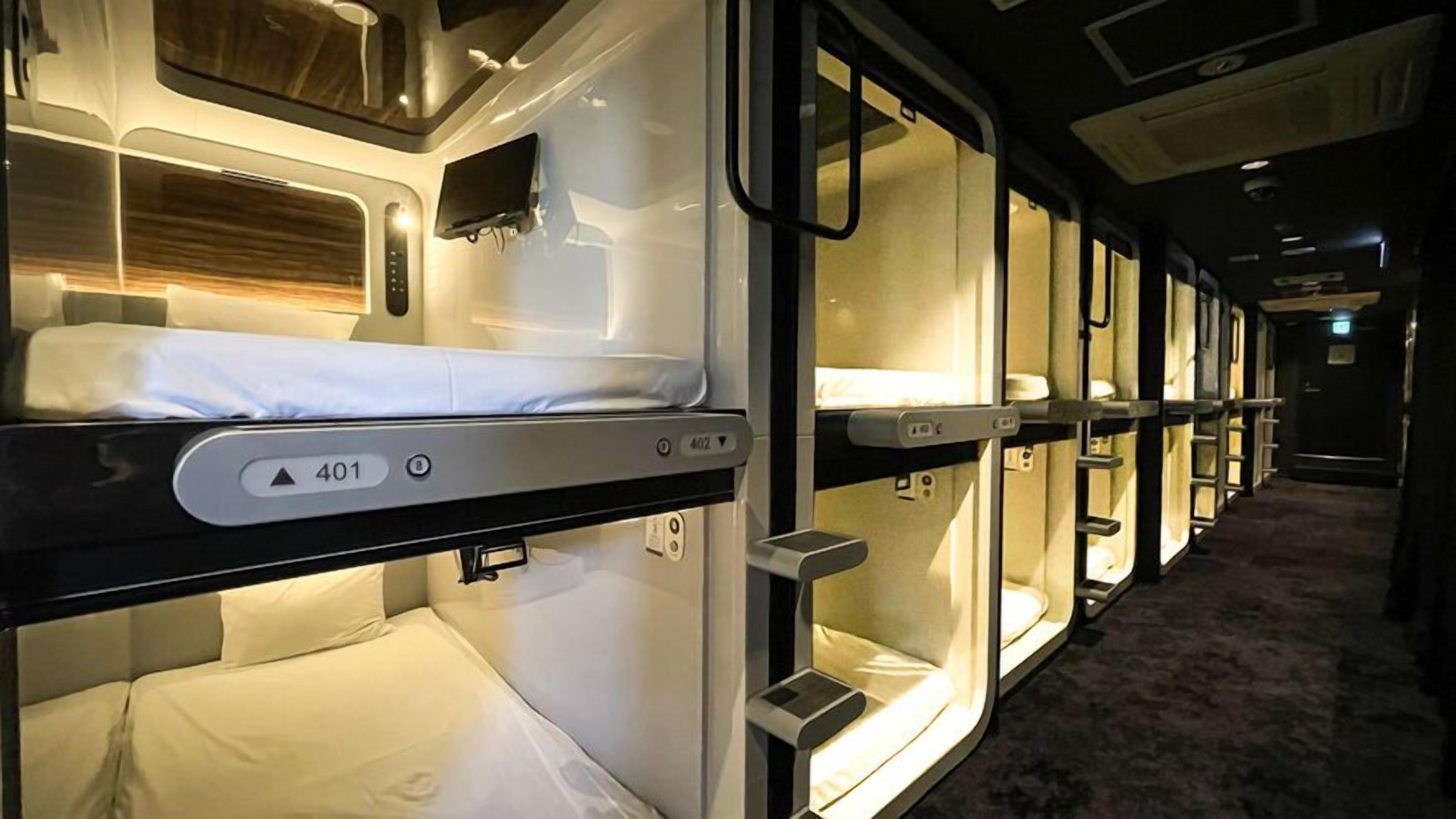 A train compartment with individual sleeping berths, each with a bed, a small table, and a personal storage space.