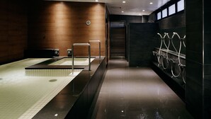 A modern bathroom with a large bathtub, a shower area with multiple faucets, and a dark tiled wall. - Spa & Capsule Hotel Grandpark Inn Kitasenju (Tokyo)