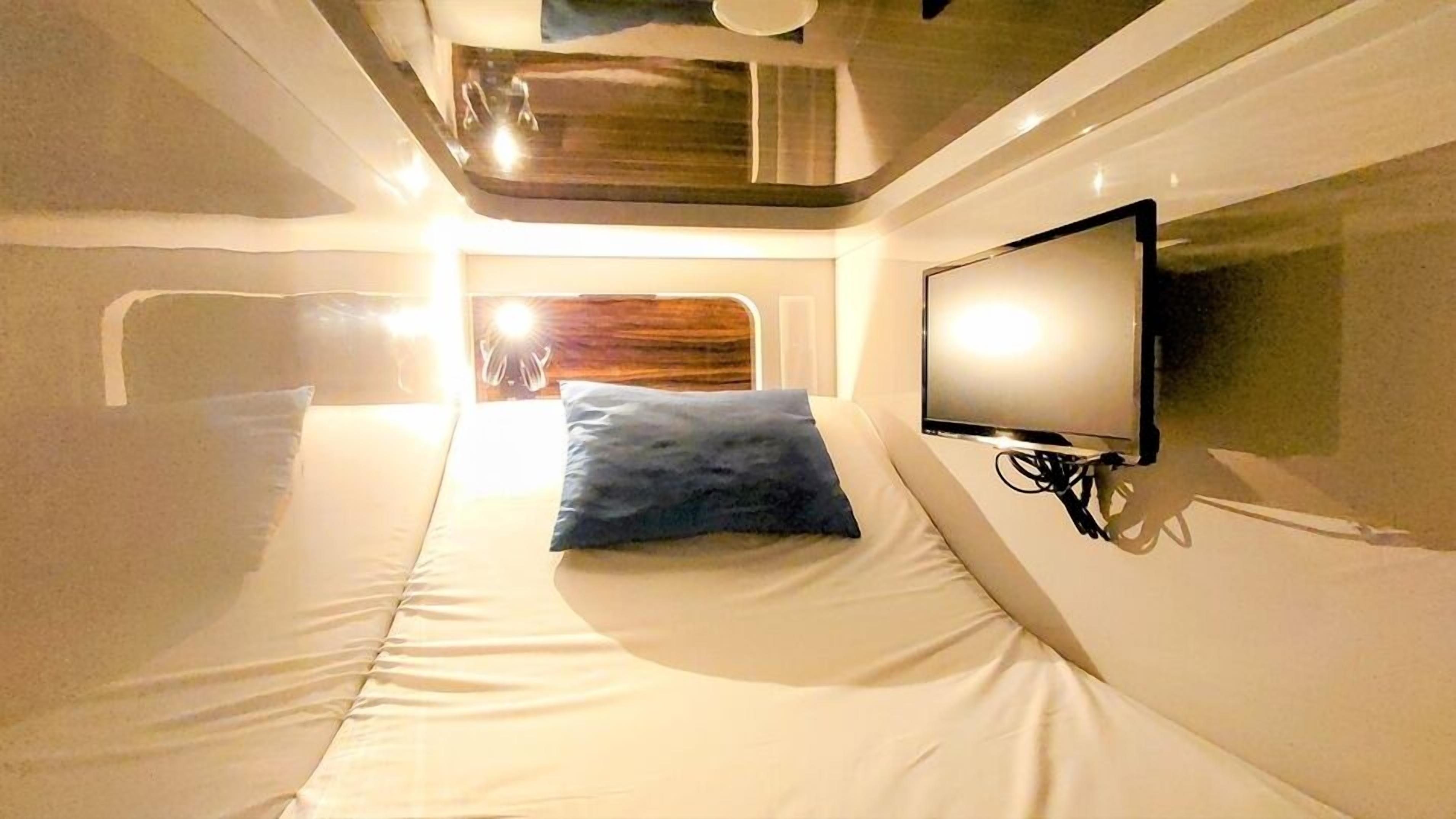 A single bed with a blue pillow, a wall-mounted TV, and a wooden headboard.