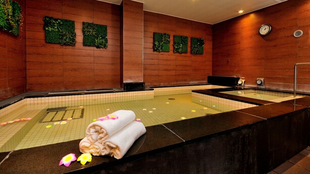 A spa area with a large hot tub, wooden walls, and green wall decorations. - Spa & Capsule Hotel Grandpark Inn Kitasenju (Tokyo)