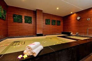 A spa area with a large hot tub, wooden walls, and green wall decorations. - Spa & Capsule Hotel Grandpark Inn Kitasenju (Tokyo)
