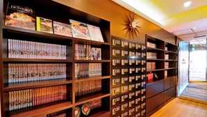 A library with bookshelves and a wall of numbered storage boxes. - Spa & Capsule Hotel Grandpark Inn Kitasenju (Tokyo)