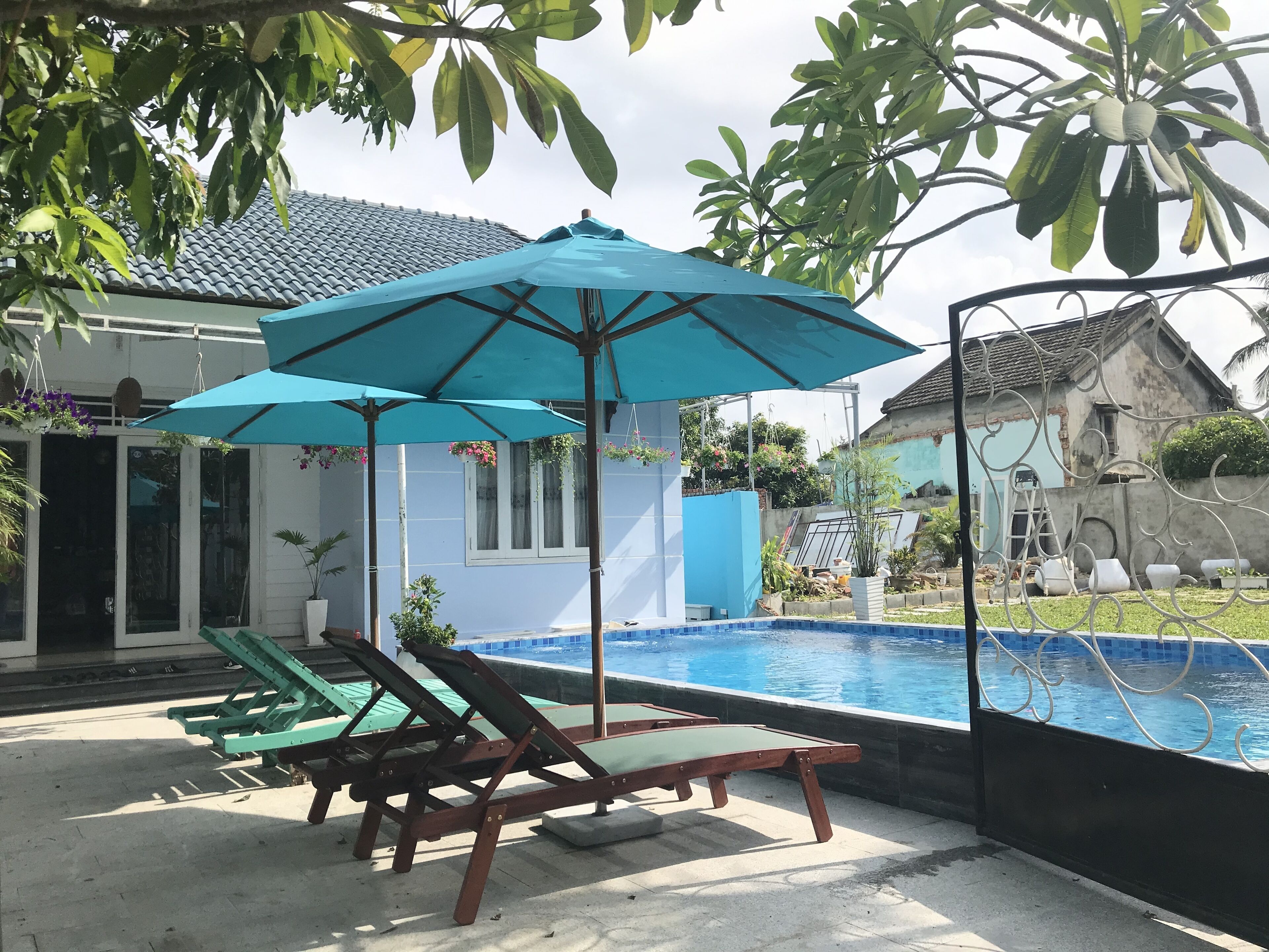 A poolside area with lounge chairs and umbrellas, a tiled roof, and a view of a house in the background.