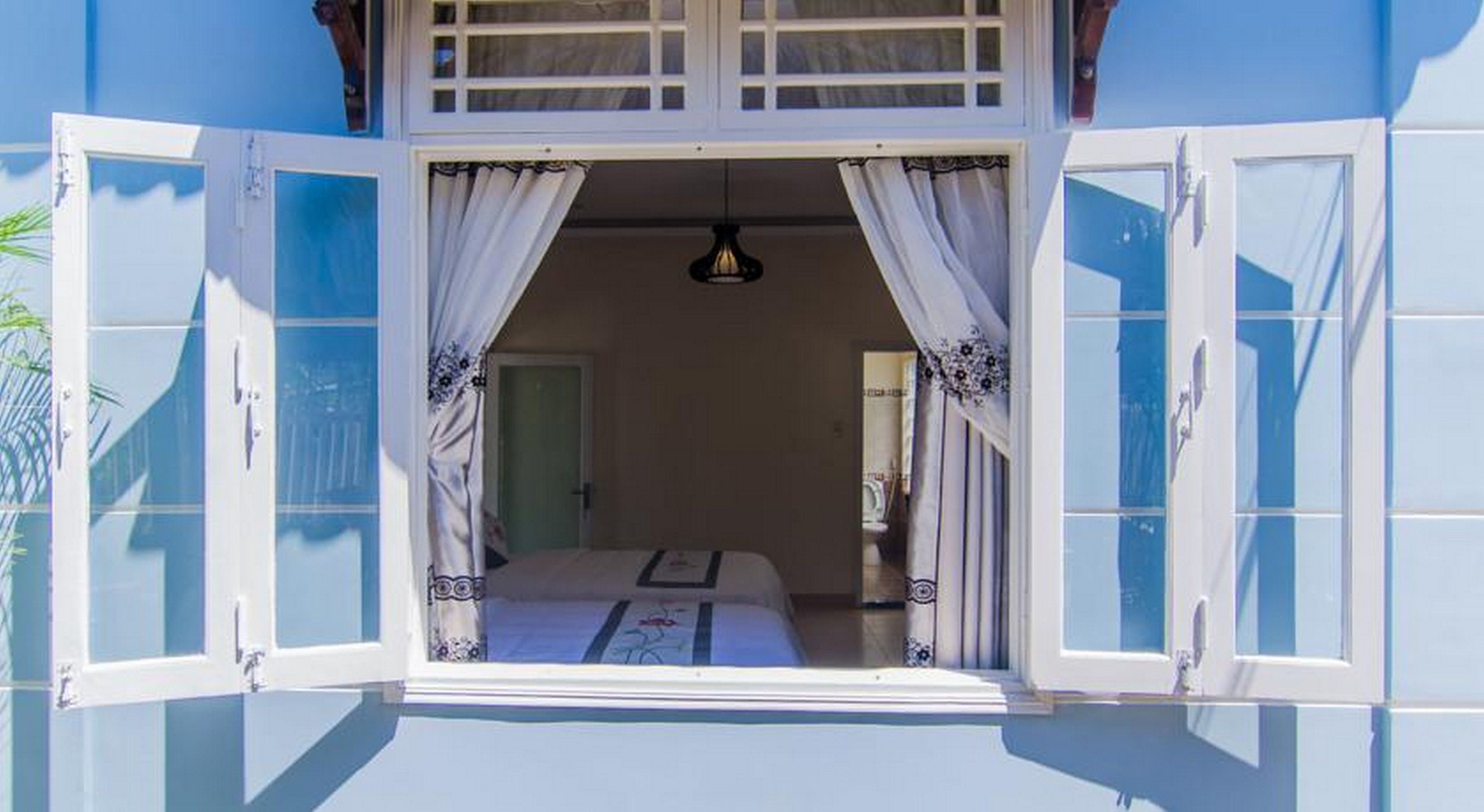 A room with a bed, a hanging light fixture, and a view through open curtains.